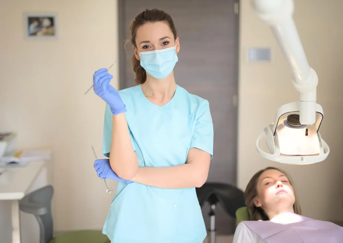Dental professional wearing a mask and gloves standing beside a patient in a dental chair, prepared for an IV dental sedation appointment.