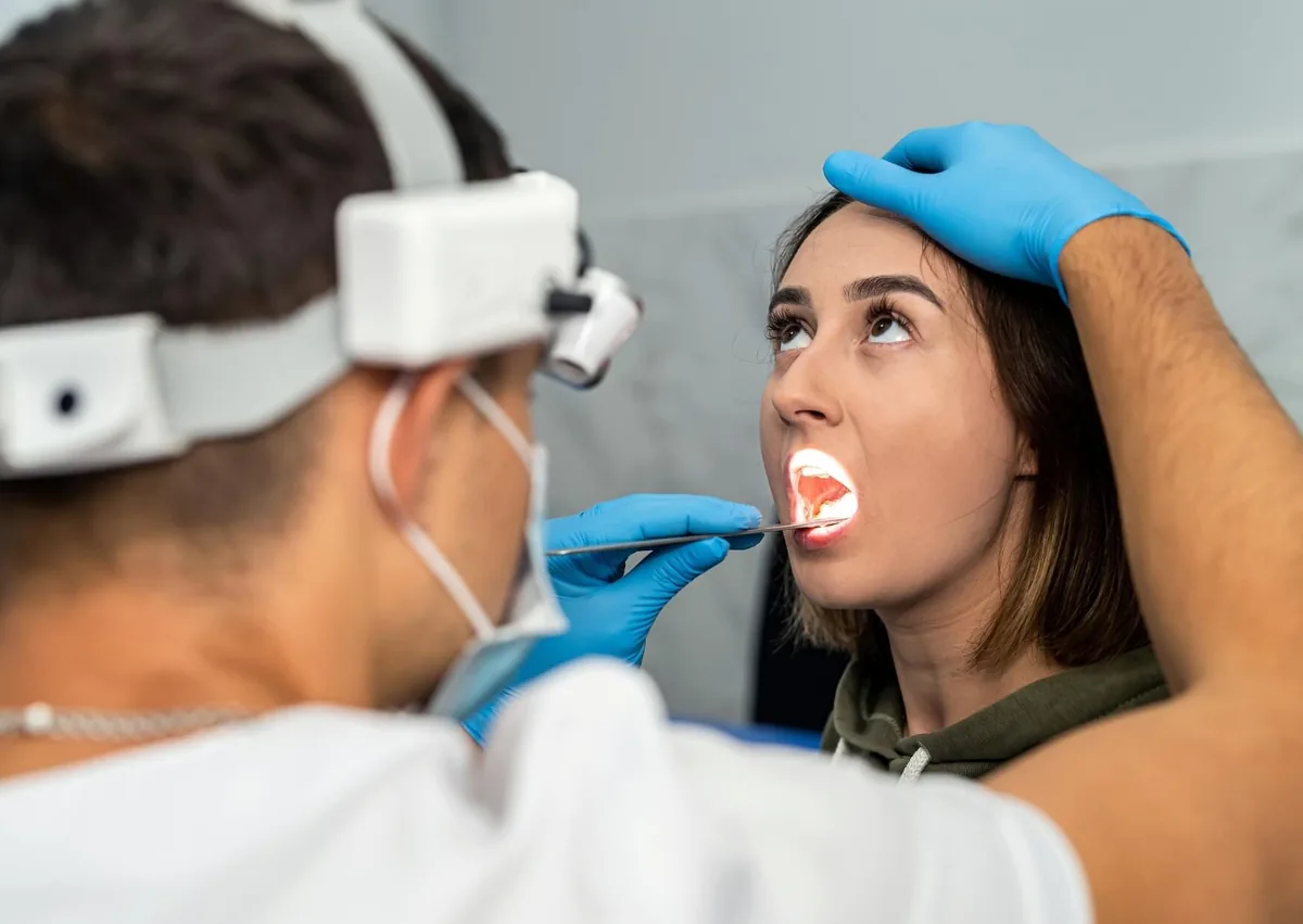 Healthcare professional examining a patient's mouth and tongue for signs of oral thrush using a light and dental instrument.